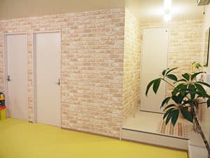 レンガ調の壁と白い扉、黄色い床の廊下(更衣室・シャワー室エリア)