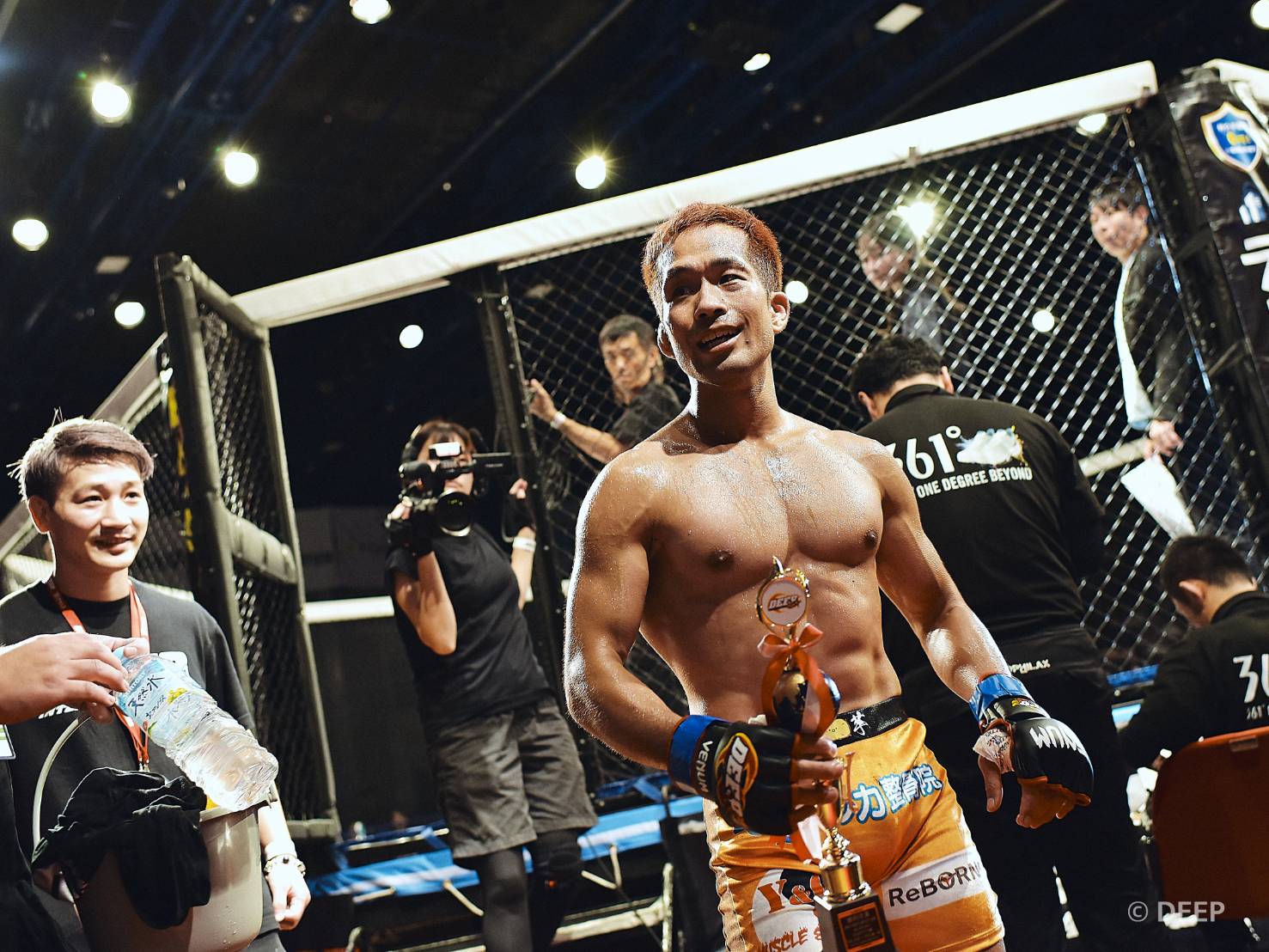 MMA試合後、リング上でトロフィーを掲げて勝利を祝う平井トレーナー